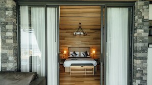 A bedroom with a bed, bedside lamps, a wooden headboard, and a stone accent wall. - Sea&Sky luxury absolute beachfront villa (Koh Samui)
