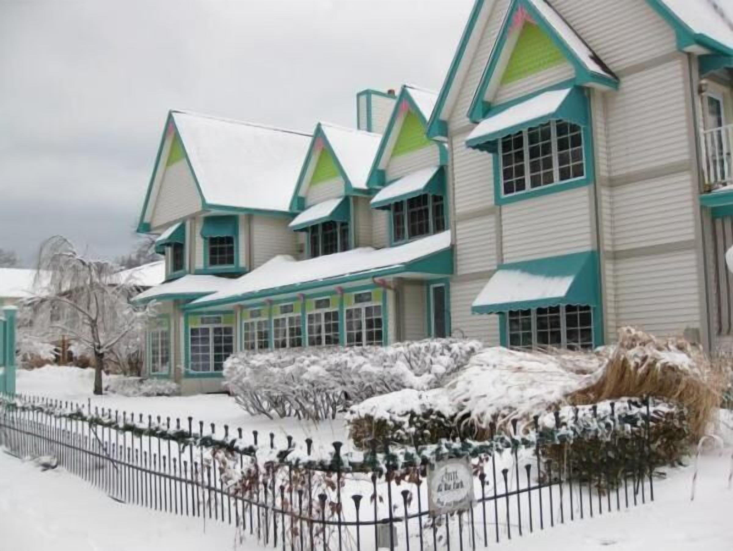 A large, multi-story house with a snow-covered roof and a fenced yard.
