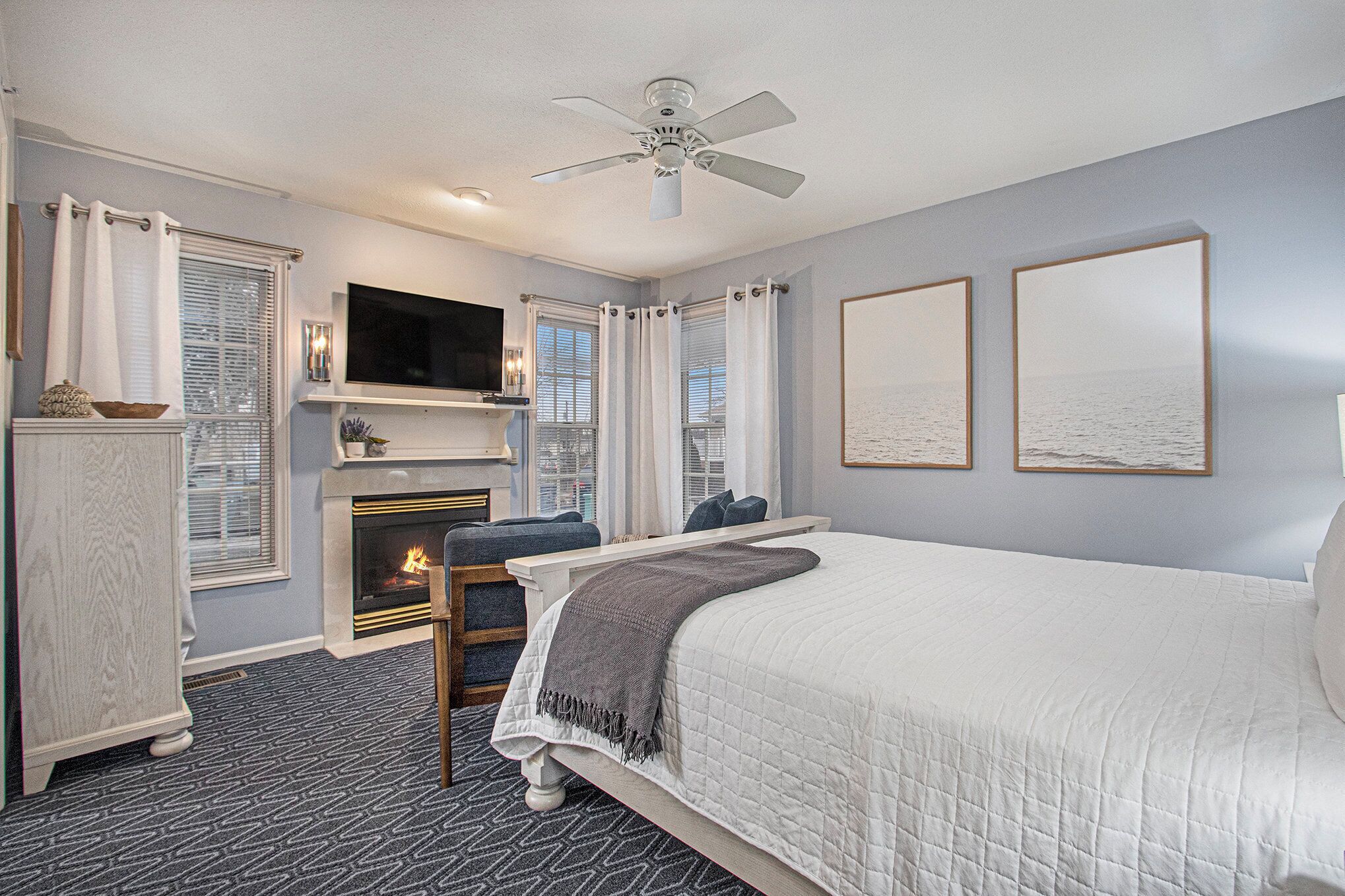 A bedroom with a bed, a fireplace, a television, and a ceiling fan.