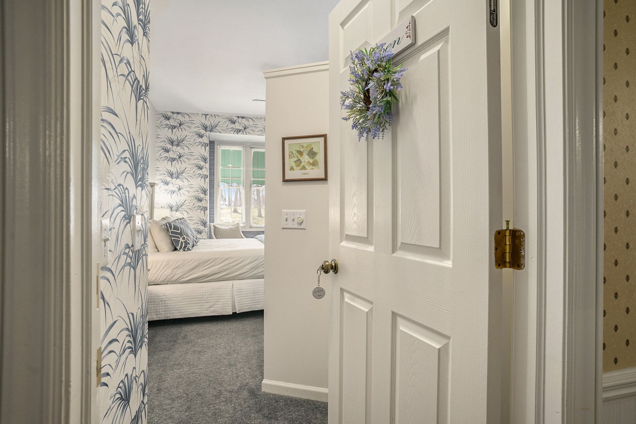 A room with a bed, a door with a keyhole, and a wall with a framed picture.