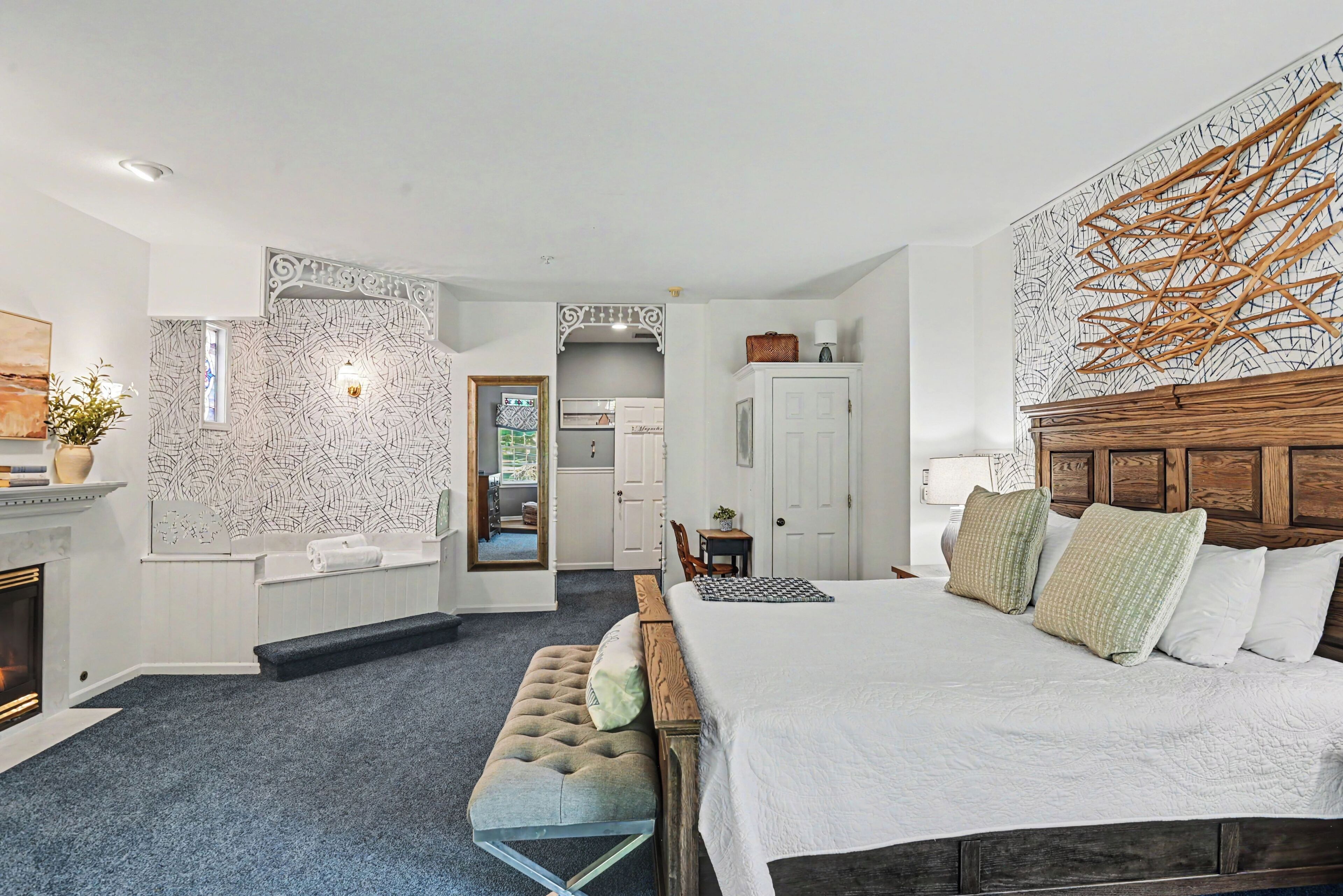 A bedroom with a large bed, a bench, a fireplace, and a wall with a unique pattern.