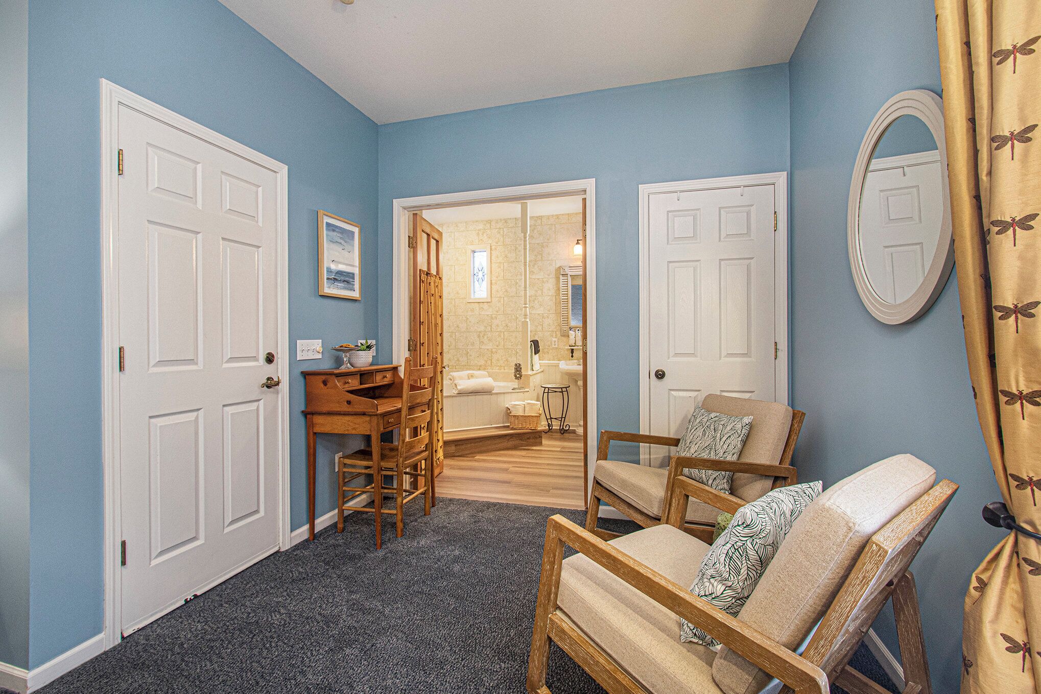 Una habitación con pared azul, un escritorio de madera, una silla y una puerta que da a un baño.