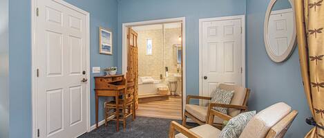 Una habitación con pared azul, un escritorio de madera, una silla y una puerta que da a un baño.