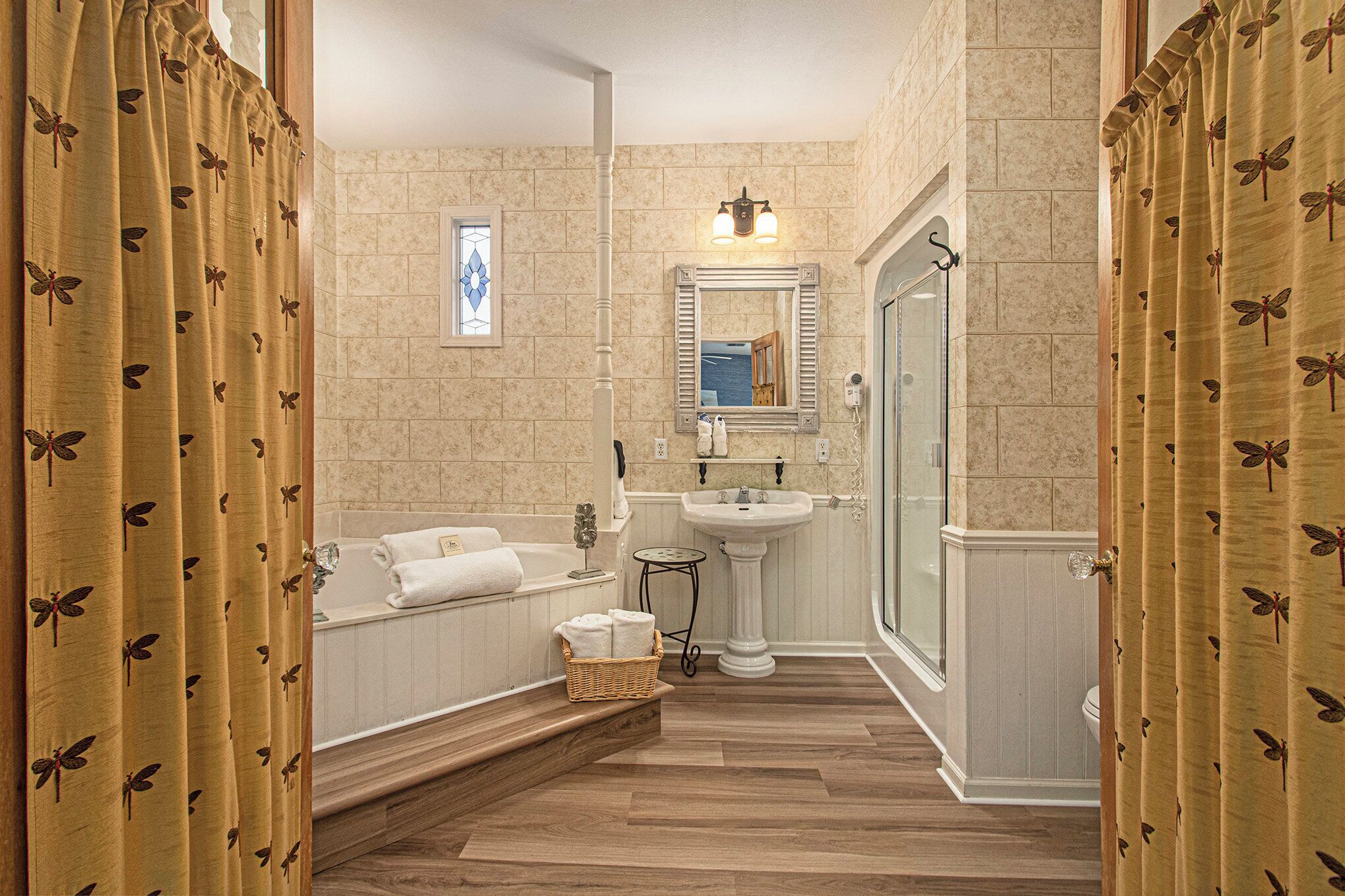 A bathroom with a bathtub, sink, and shower. There is a mirror above the sink and a window with a view of the outside.
