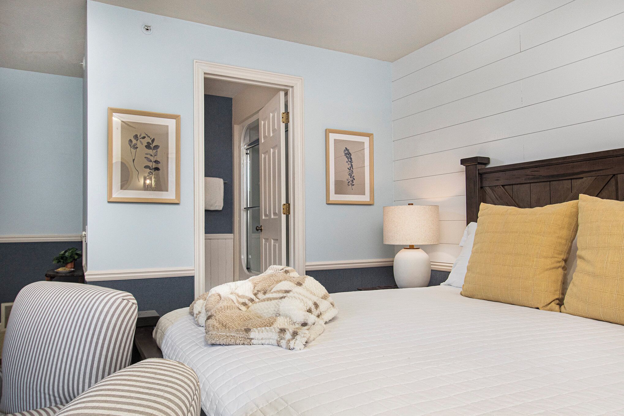 Une chambre d’hôtel avec un lit, une chaise, une lampe et deux tableaux encadrés au mur.
