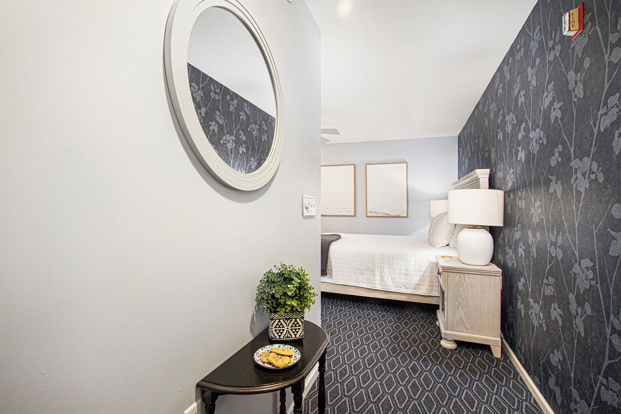 Una habitación de hotel con una cama, una mesita de noche con una lámpara, una pequeña mesa con una planta y un espejo en la pared.