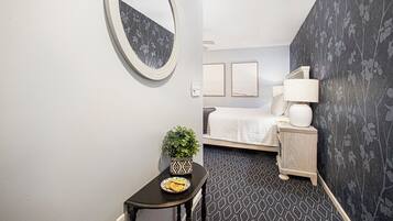 Una habitación de hotel con una cama, una mesita de noche con una lámpara, una pequeña mesa con una planta y un espejo en la pared.