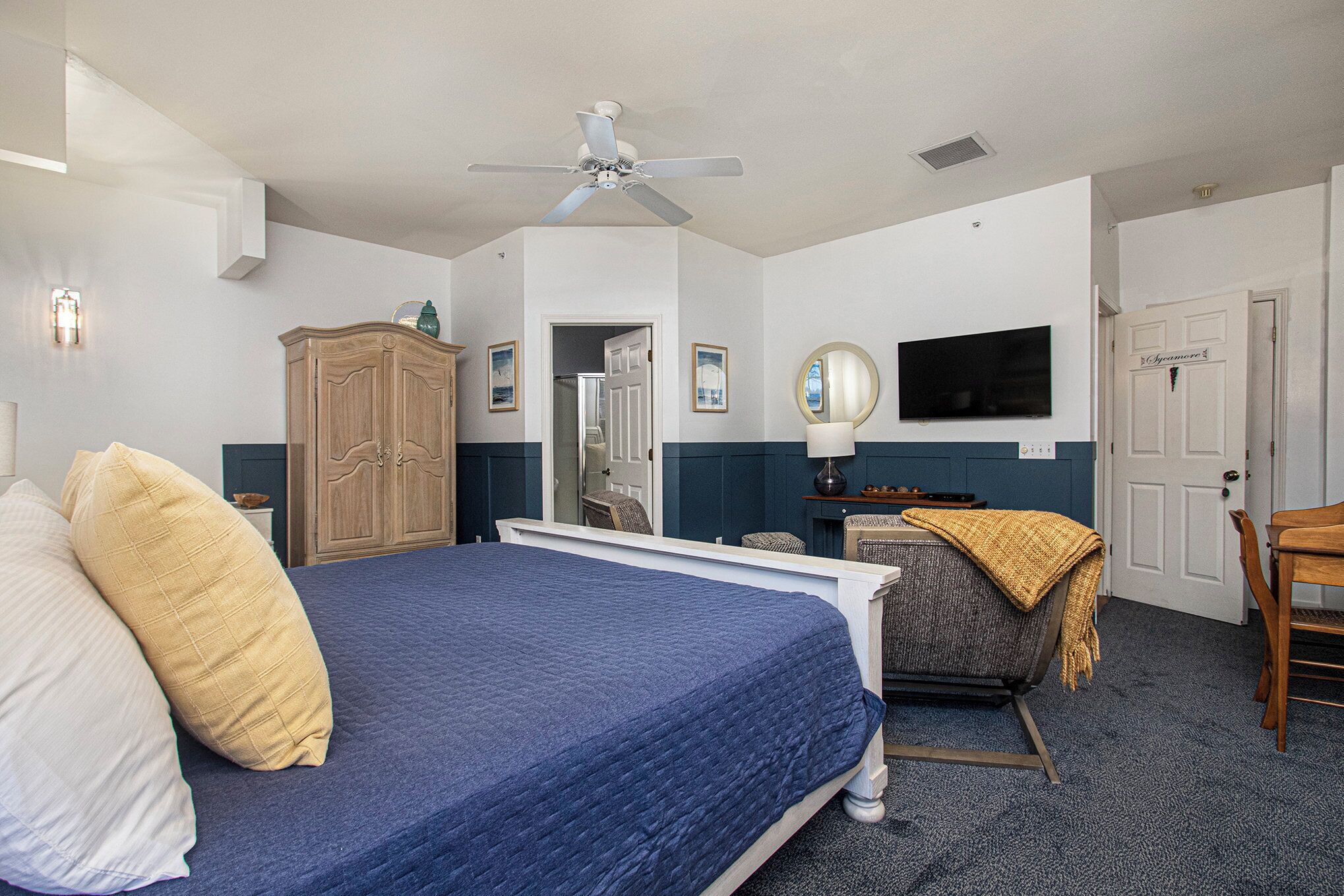 A hotel room with a bed, a desk, a chair, a wardrobe, a television, and a ceiling fan.