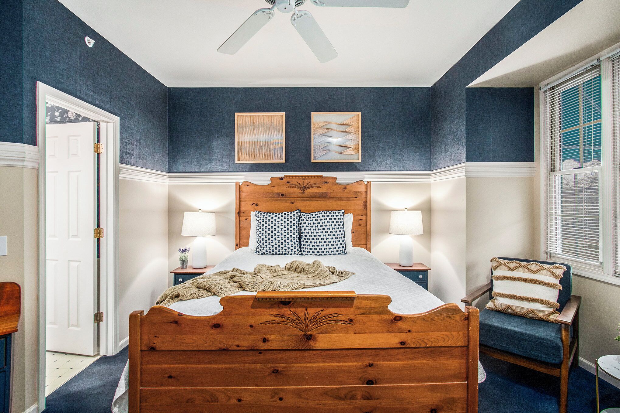 A bedroom with a wooden bed, two wall-mounted lamps, a ceiling fan, and a window with blinds.