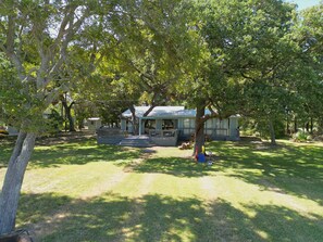 A house with a large tree in front, a covered porch, and a grassy yard.