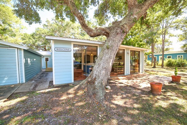 A small, single-story building with a 'Welcome' sign, a covered porch, and a tree in front.