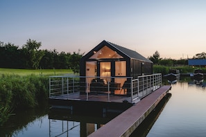 Una casa flotant moderna amb façana de vidre, una coberta i una petita zona d'estar a l'exterior.