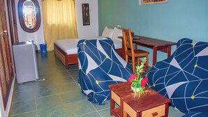 Ein Zimmer mit einem Bett, zwei Sofas, einem kleinen Tisch mit Blumen, einem Schreibtisch, einem Stuhl, einem Fenster mit Vorhängen und einem Wandbild.