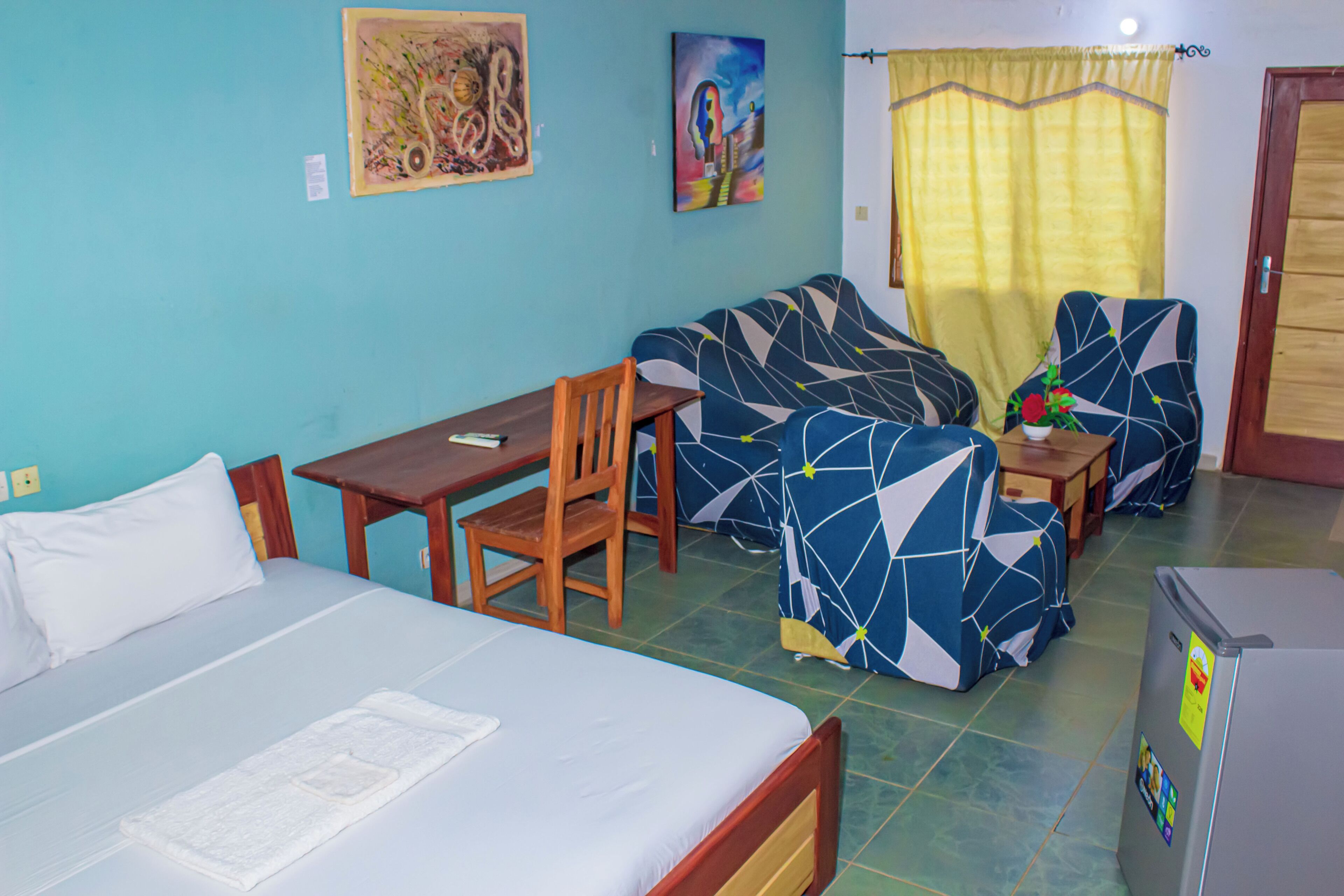 A room with a bed, a desk, a chair, a sofa, and a small table. There are two paintings on the wall.
