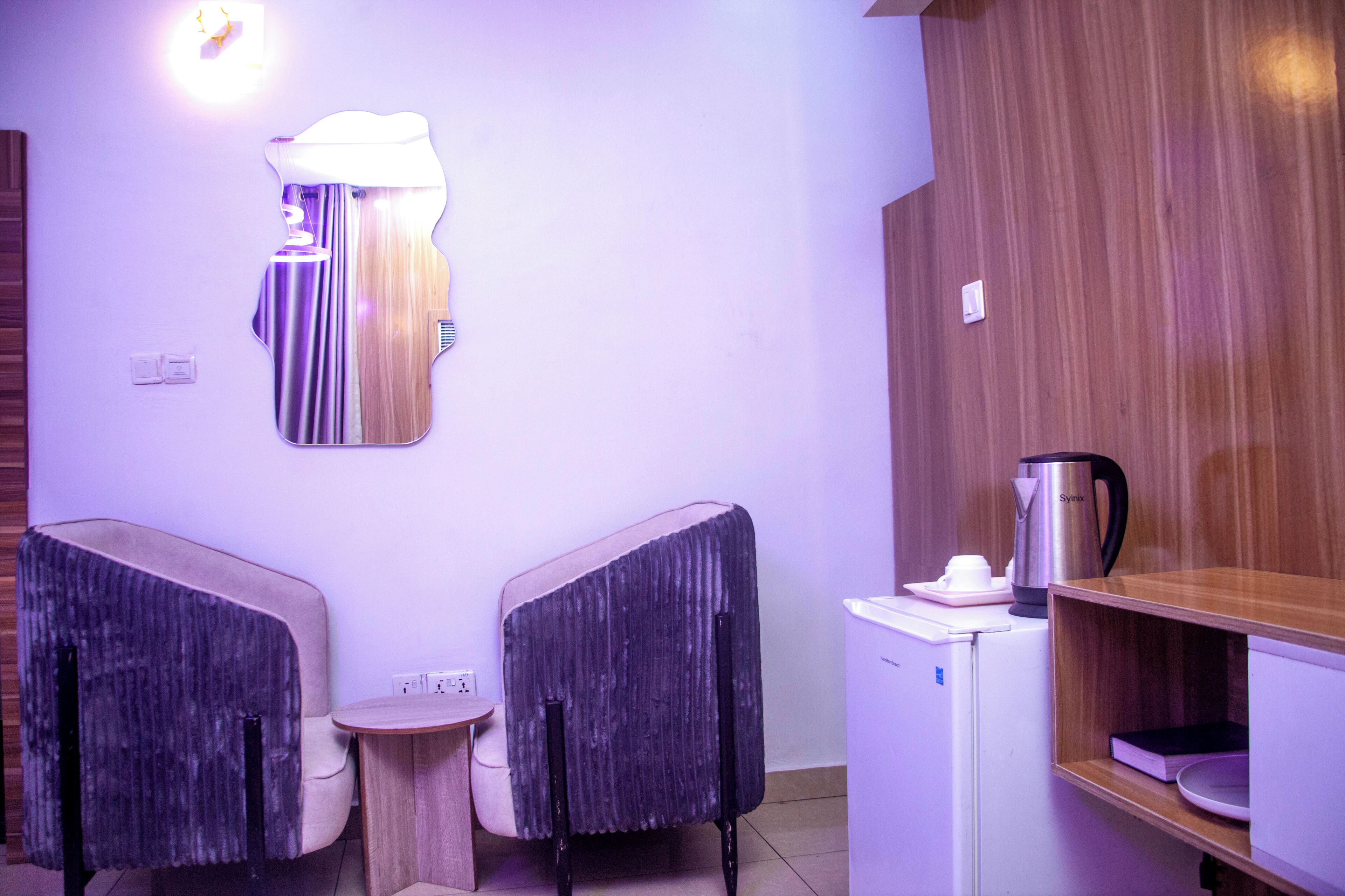 A room with two chairs, a small table, a kettle, a coffee maker, and a white refrigerator.