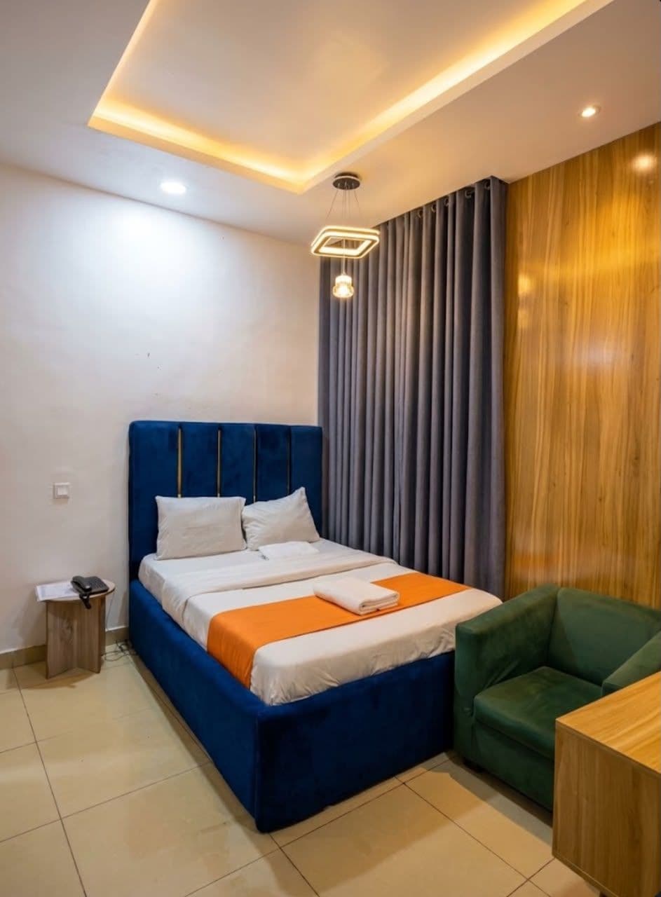 A modern hotel room with a bed, a green chair, and a wooden table.