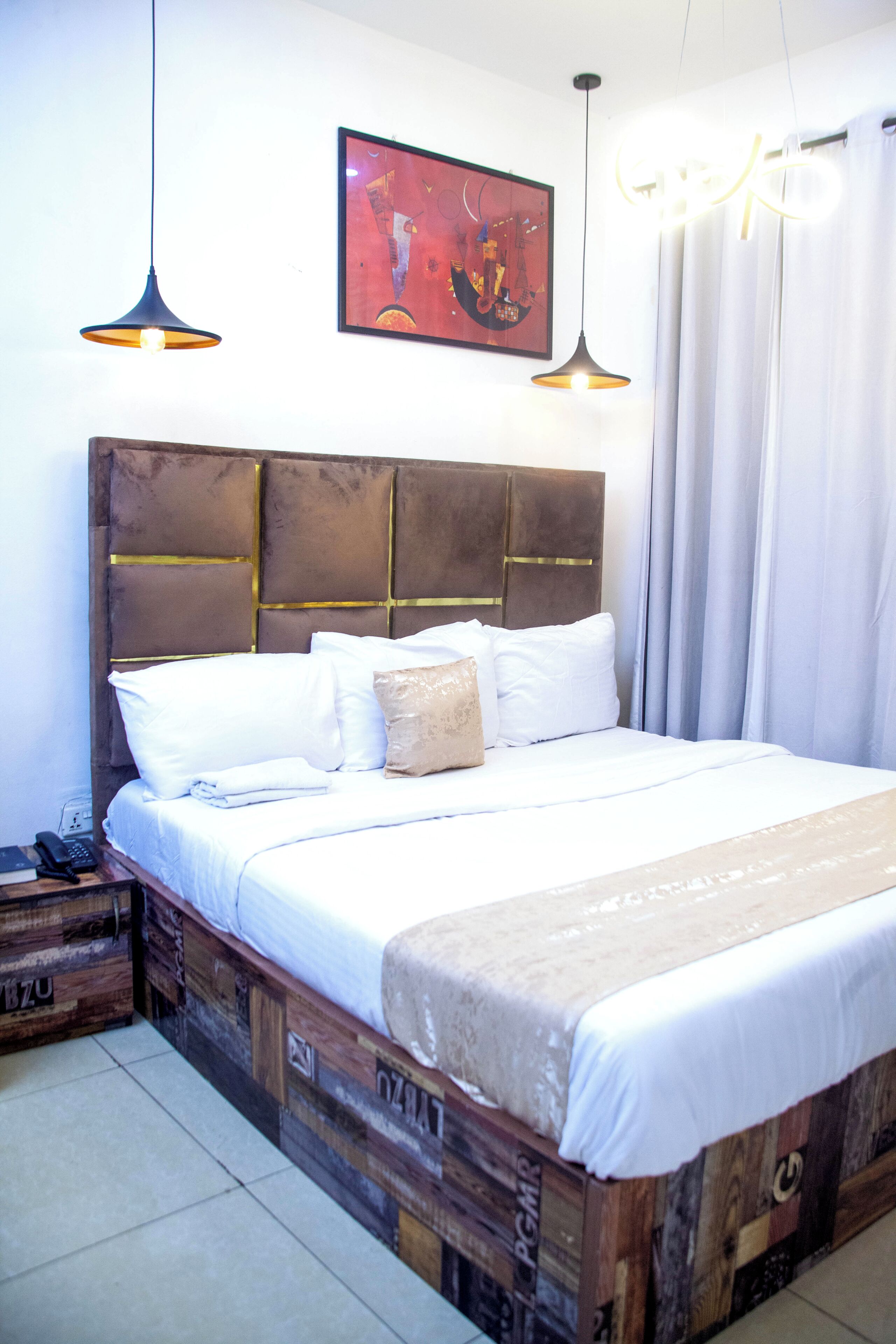 A bed with a wooden headboard, white bedding, and two pendant lights.