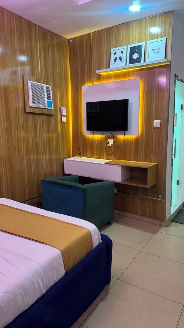 A hotel room with a bed, a TV mounted on a wooden wall, a small desk, and a wardrobe.