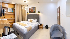 Una habitación de hotel con cama, mesita de noche, lámpara, silla y un cuadro en la pared.