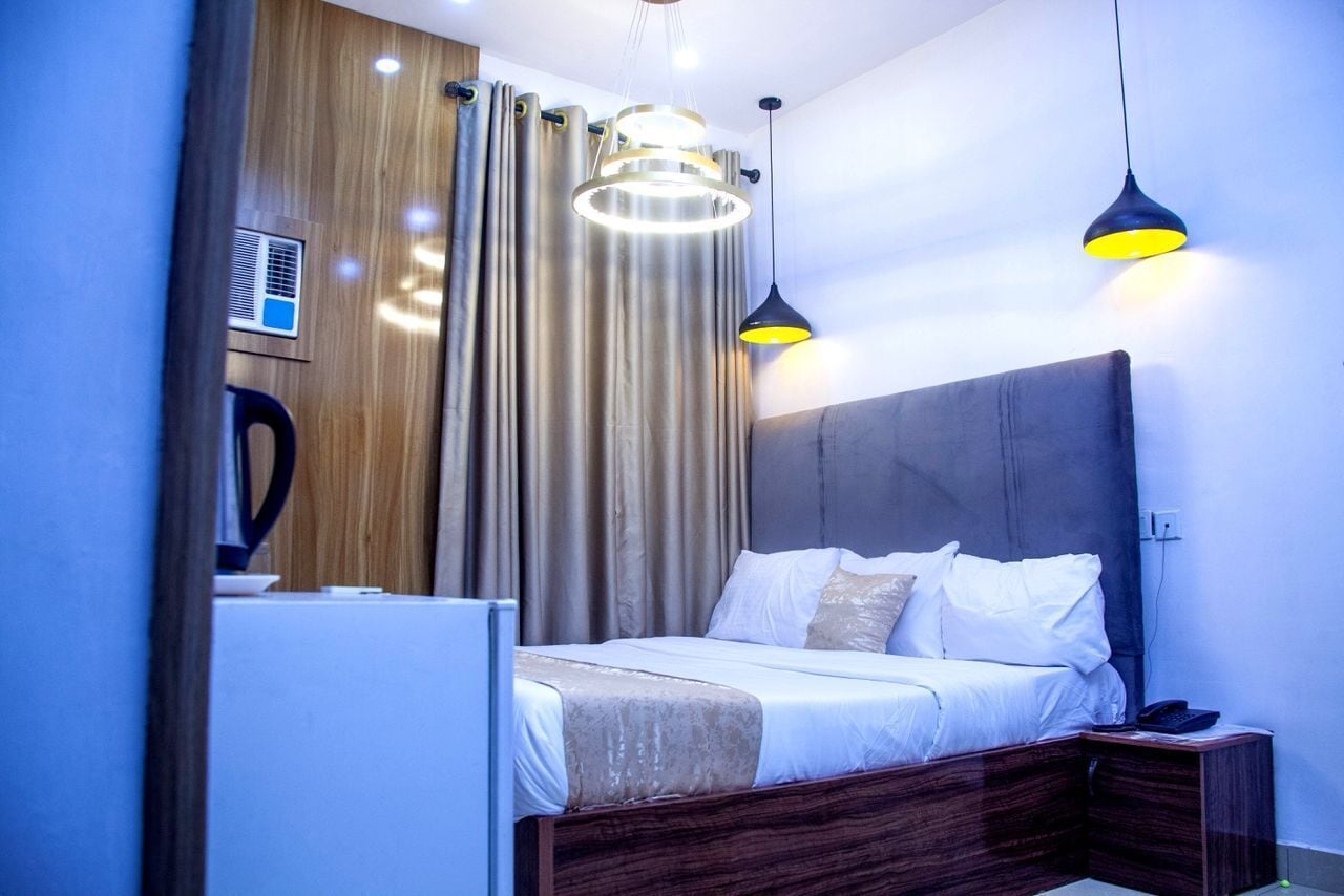 Ein modernes Schlafzimmer mit einem hölzernen Kopfteil, einem Bett mit weißer Bettwäsche und zwei Pendelleuchten.