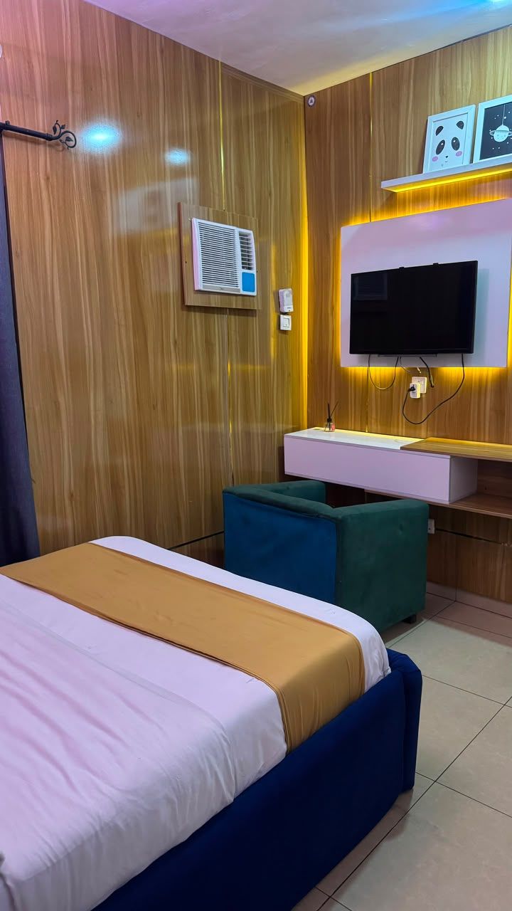 A hotel room with a bed, a desk, a television, and a wall-mounted air conditioning unit.