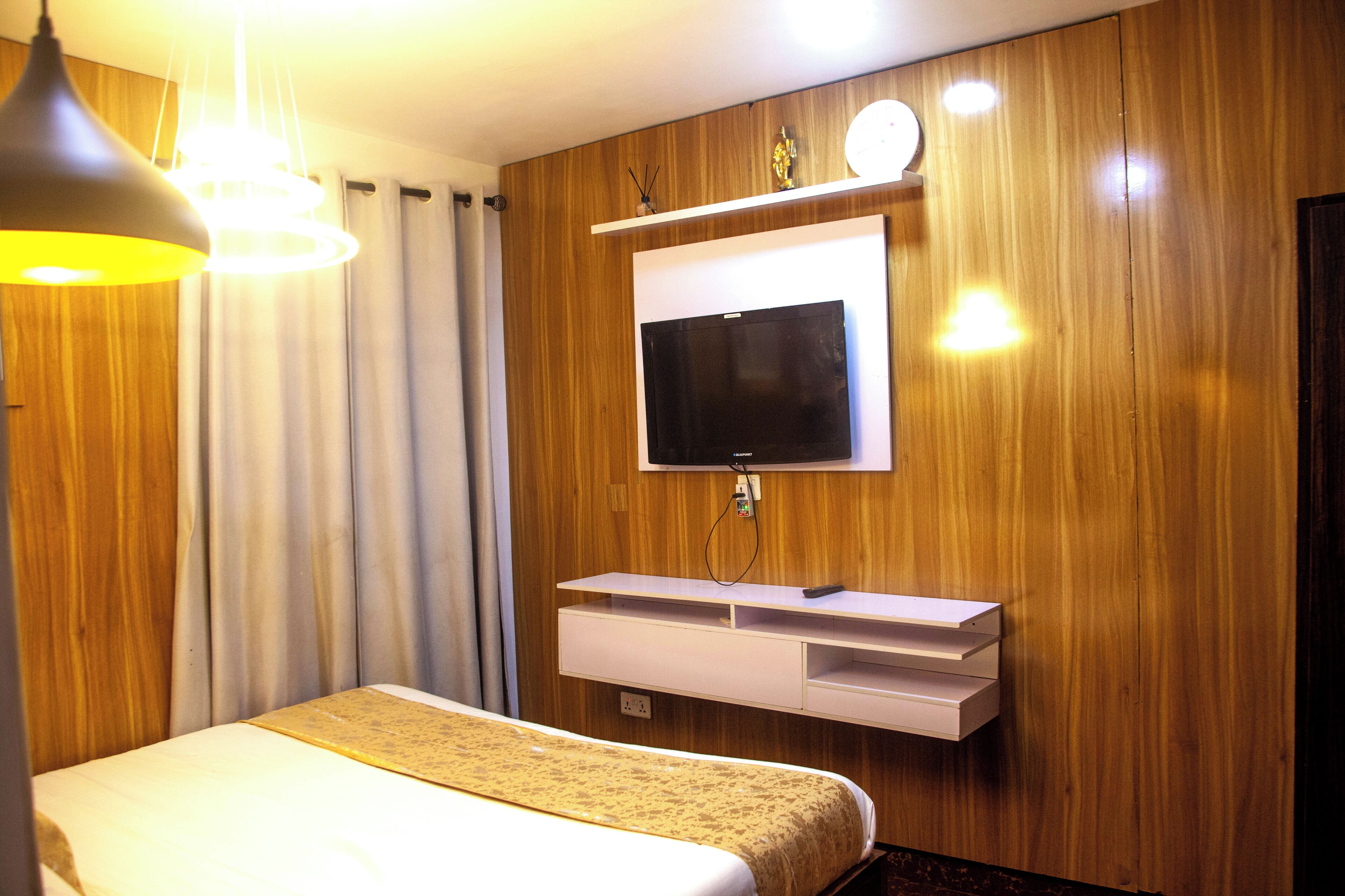 Een hotelkamer met een bed, een wandtelevisie, een nachtkastje en een houten wand.