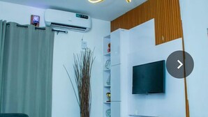 Una sala de estar moderna con un televisor de pantalla plana montado en una pared blanca, un sofá gris y una lámpara decorativa.