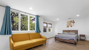 A modern bedroom with a wooden floor, a yellow sofa, a bed with a grey duvet, and a window with teal curtains. - Beachfront 4BR - 30ft to Sand •Near Amusement Park (Keansburg)