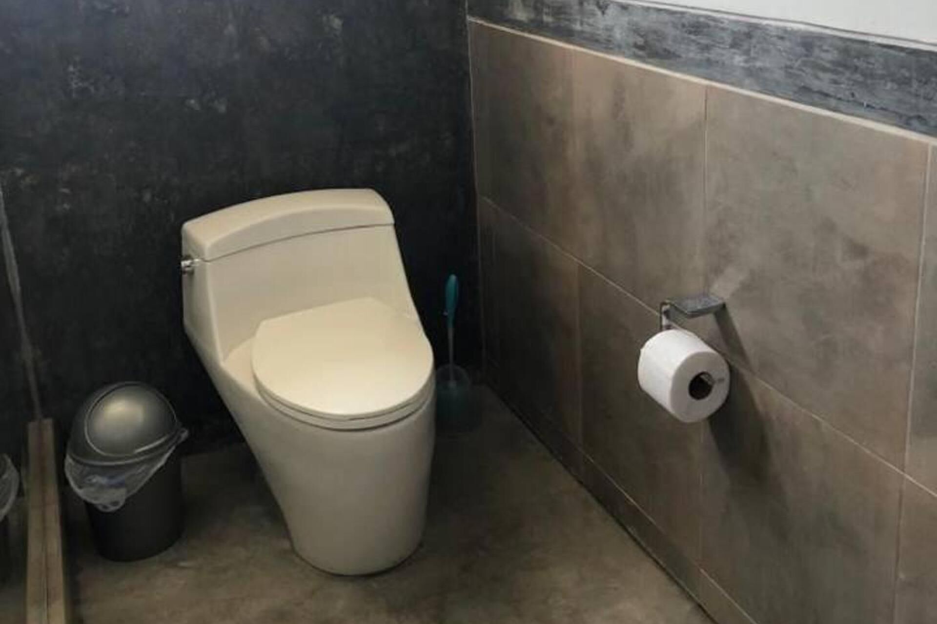 Une petite salle de bain compacte, équipée de toilettes, d’une poubelle et d’un porte-rouleau de papier toilette fixé au mur.