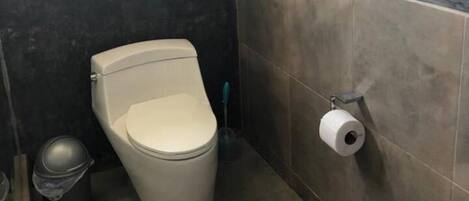 A small, compact bathroom with a toilet, a trash bin, and a toilet paper holder on the wall.
