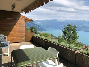 Un balcón con mesa y sillas, con vistas a un lago y montañas.