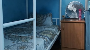 Ein Schlafraum mit Etagenbetten, einer Bettdecke mit Muster, einem hölzernen Schrank und einem Wandventilator.
