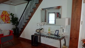 Un escalier avec une finition en bois et des balustrades noires, une console en verre avec un miroir, une horloge et une bouteille de vin.