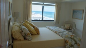 Un dormitorio con cama, ventana con vista al mar, una silla y una lámpara.