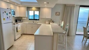 Una cocina moderna con muebles blancos, una isla central y vistas al mar a través de un ventanal grande.