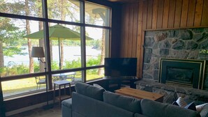 Un salon chaleureux avec une cheminée en pierre, une grande fenêtre donnant sur l’extérieur et un canapé confortable.