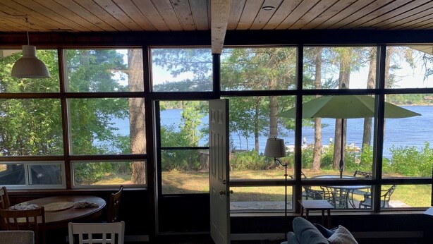 Une pièce dotée de grandes fenêtres donnant sur un lac, un coin repas avec une table et des chaises, et un espace détente avec un canapé.