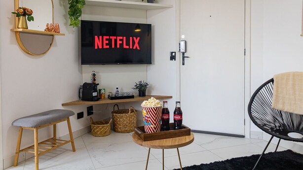 A living room with a TV displaying 'NETFLIX', a coffee machine, popcorn, and two Coca-Cola bottles on a table.