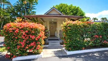 A two-story building with a covered entrance, surrounded by lush greenery and flowering bushes.