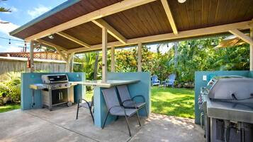 An outdoor patio with a covered grill area, two chairs, and a table.