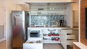 A modern kitchen with a built-in refrigerator, a microwave, and a coffee maker. - Condomínio Tag Decor (São Paulo)