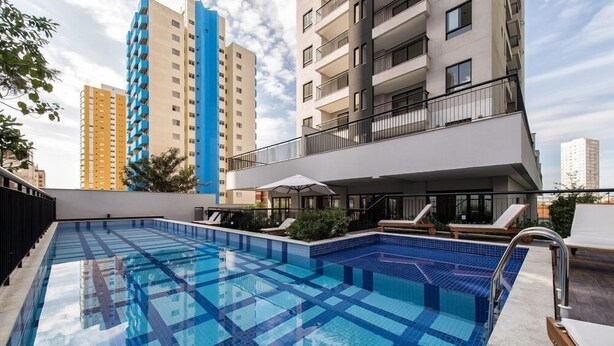 A rooftop swimming pool with lounge chairs and a view of surrounding high-rise buildings. - Condomínio Tag Decor (São Paulo)