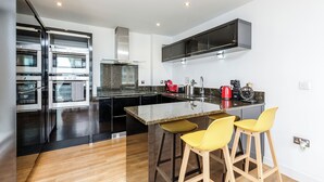 A modern kitchen with built-in ovens, a central island with stools, and a microwave above the island. - 2-Bedroom Duplex Bliss steps from Excel London (London)