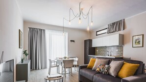 A modern living room with a sofa, dining table, and chairs. There is a kitchen area with cabinets and a tiled backsplash. - Venuto Homes by Wonderful Italy (Catania)