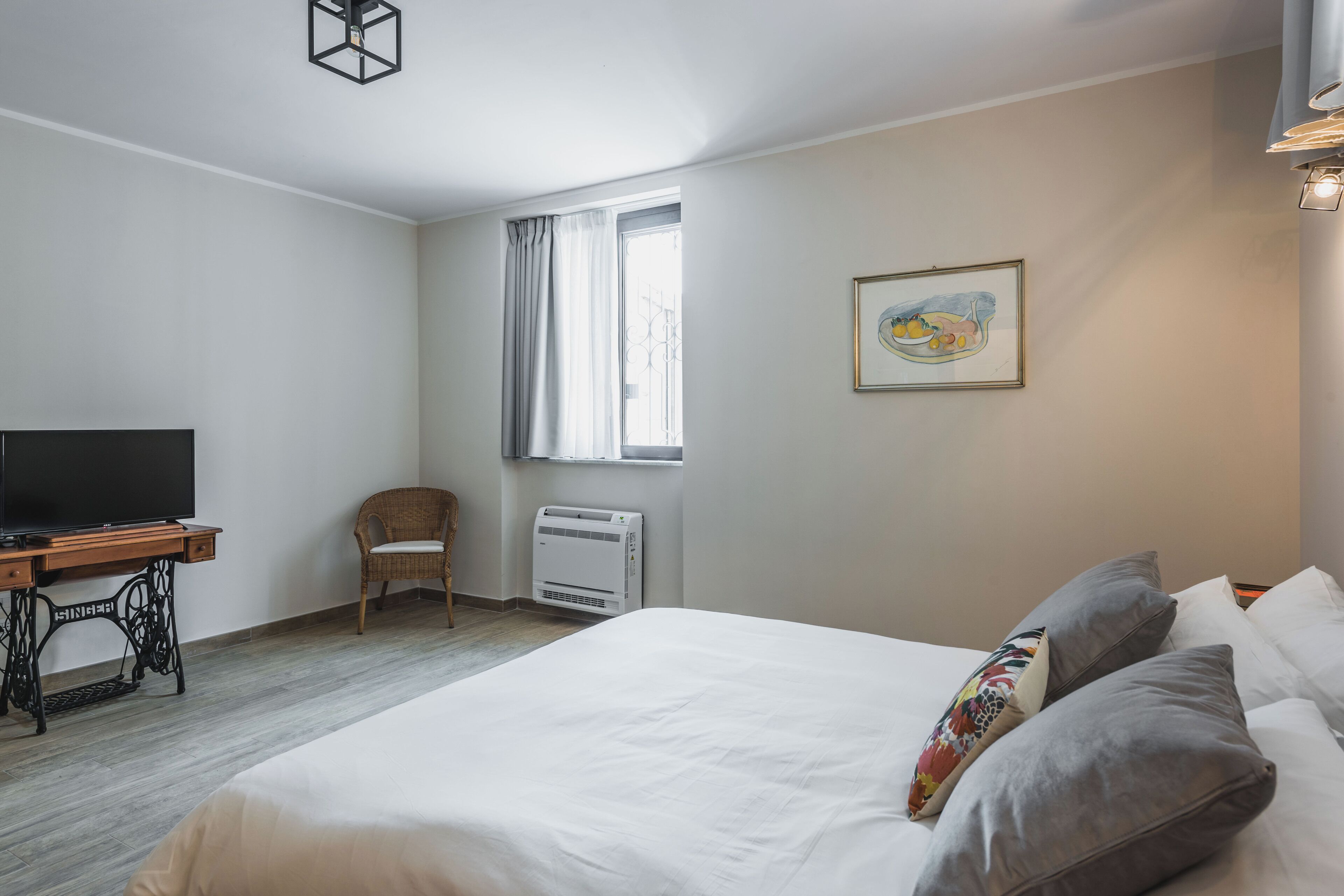A bedroom with a bed, a television, a chair, a window, and a radiator.