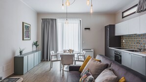 A modern living room with a grey sofa, a dining table with chairs, and a kitchen area with cabinets and a countertop. - Venuto Homes by Wonderful Italy (Catania)
