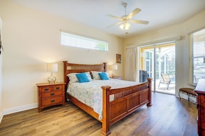 Une chambre avec un lit en bois, des tables de chevet, un ventilateur de plafond et une vue sur l’extérieur.