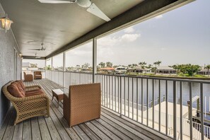 Enjoy the serene view of the water from this balcony, featuring a sofa and chair amidst palm trees and distant buildings.