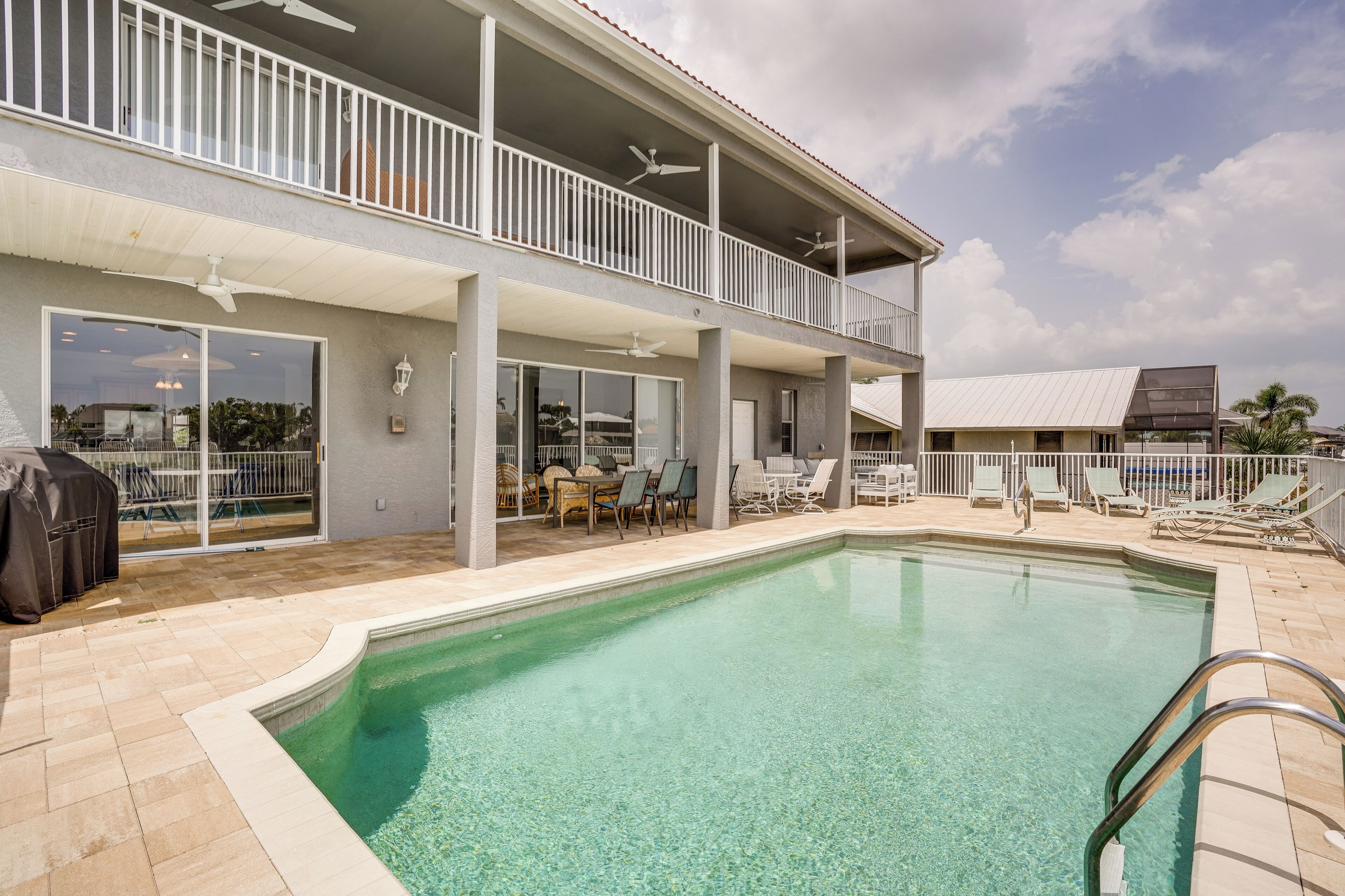 A swimming pool with a covered patio area, outdoor furniture, and a two-story building with balconies.