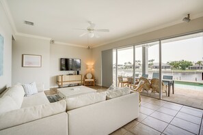 Relax in this stylish living room with a large sofa, flat-screen TV, and coffee table, offering a view of the pool and palm trees.